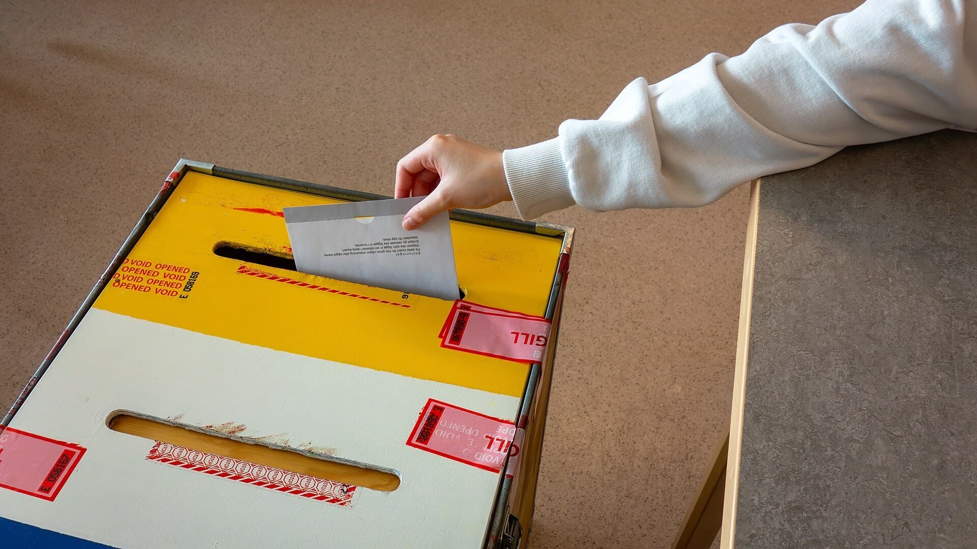 A voter's hand placing a paper ballot into a ballot box.